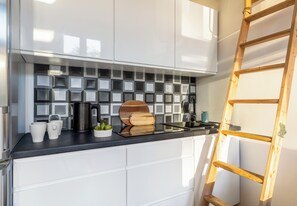A modern kitchen with white cabinets, a black countertop, and a wooden ladder leaning against the wall. - Piastów Loft Mezzanine Studio (Szczecin)
