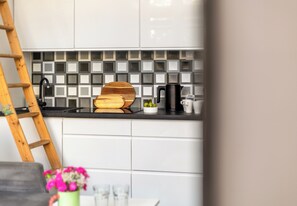 A kitchen with white cabinets, a black countertop, a wooden cutting board, a kettle, and a coffee maker. - Piastów Loft Mezzanine Studio (Szczecin)