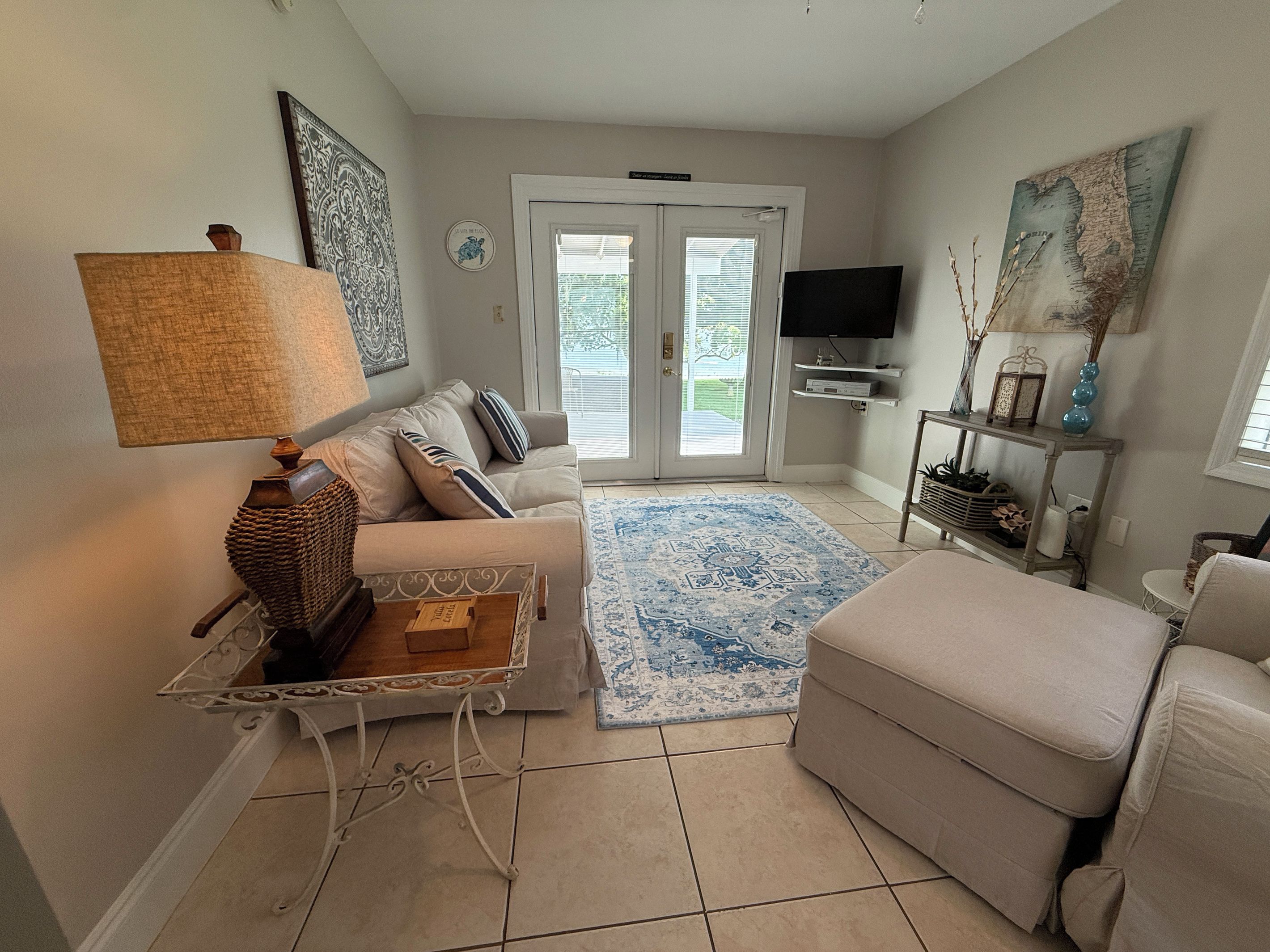 Un salon comprenant un canapé, un pouf, une table basse, une lampe, un téléviseur et des objets décoratifs.