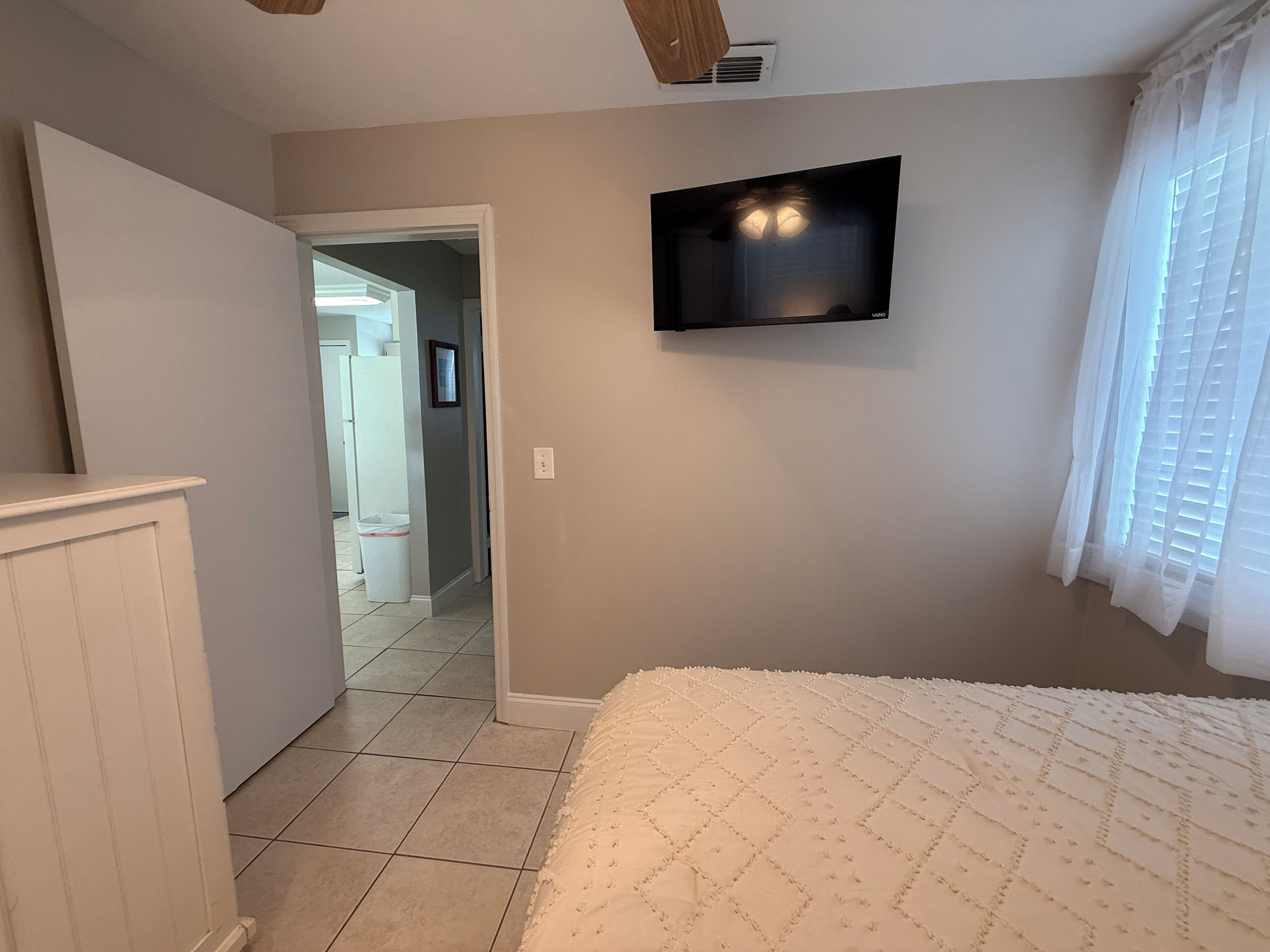 Une chambre à coucher avec un lit, un téléviseur fixé au mur et une porte donnant sur une autre pièce.
