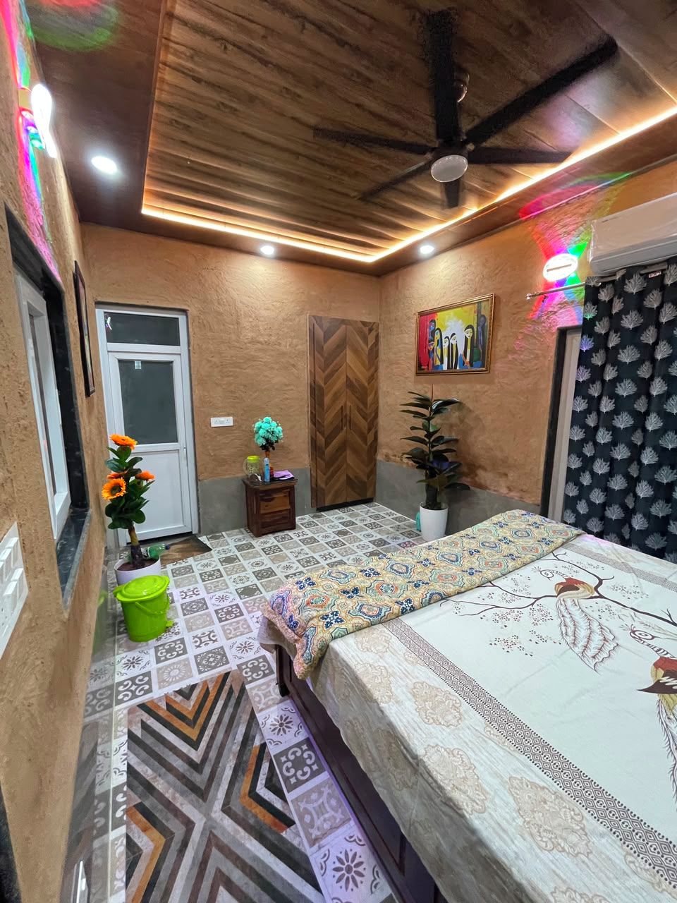 A bedroom with a bed, a ceiling fan, a door, and a wall with a painting.