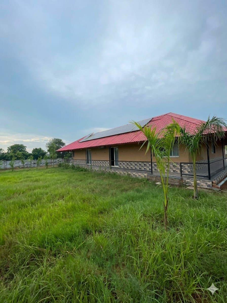 A house with a red roof, a paved area in front, and a grassy field.