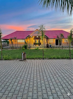 A building with a red roof, paved walkway, and small palm trees.