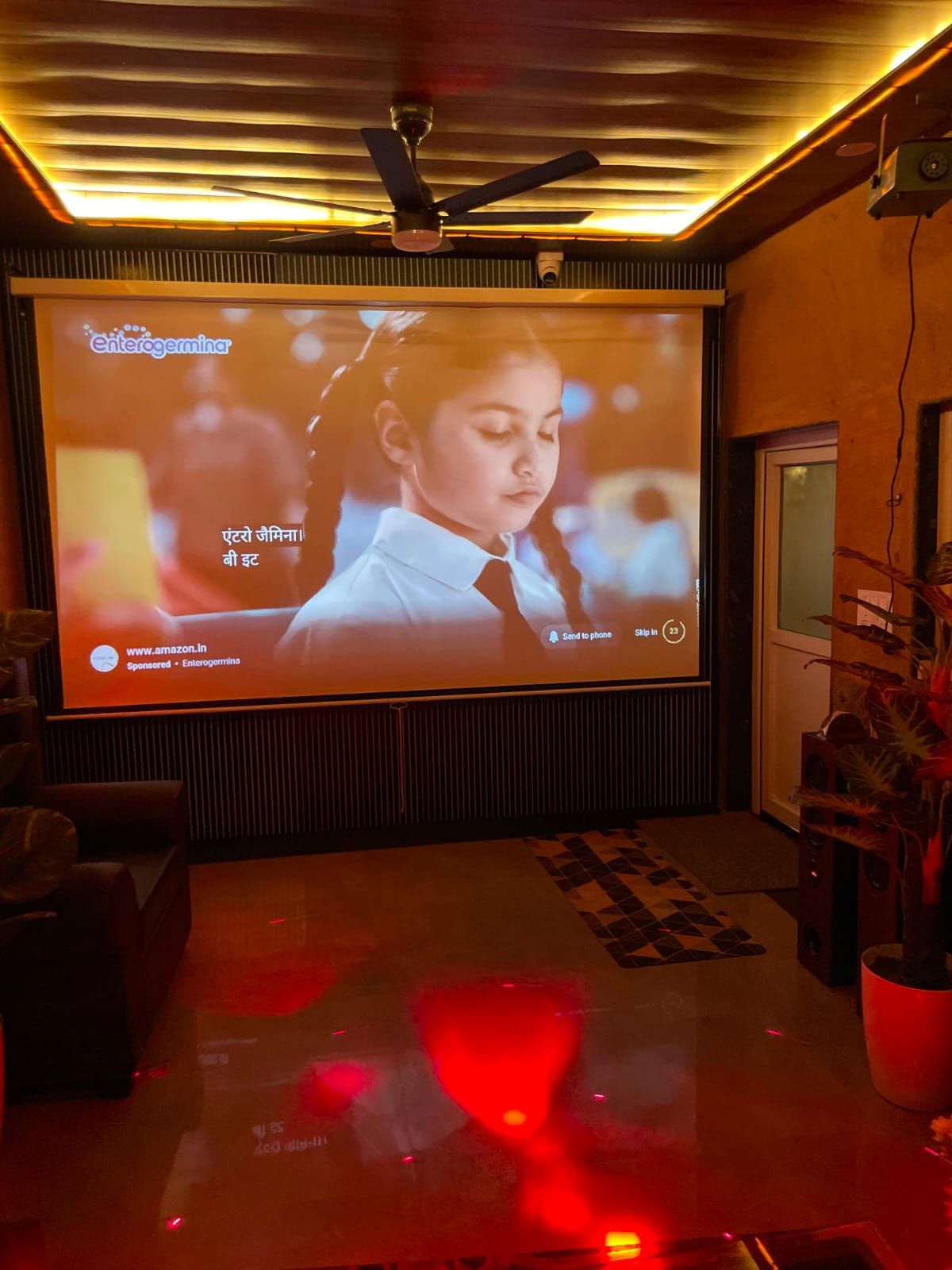 Sistema de cine en casa con una pantalla grande, ventilador de techo y una planta en maceta.