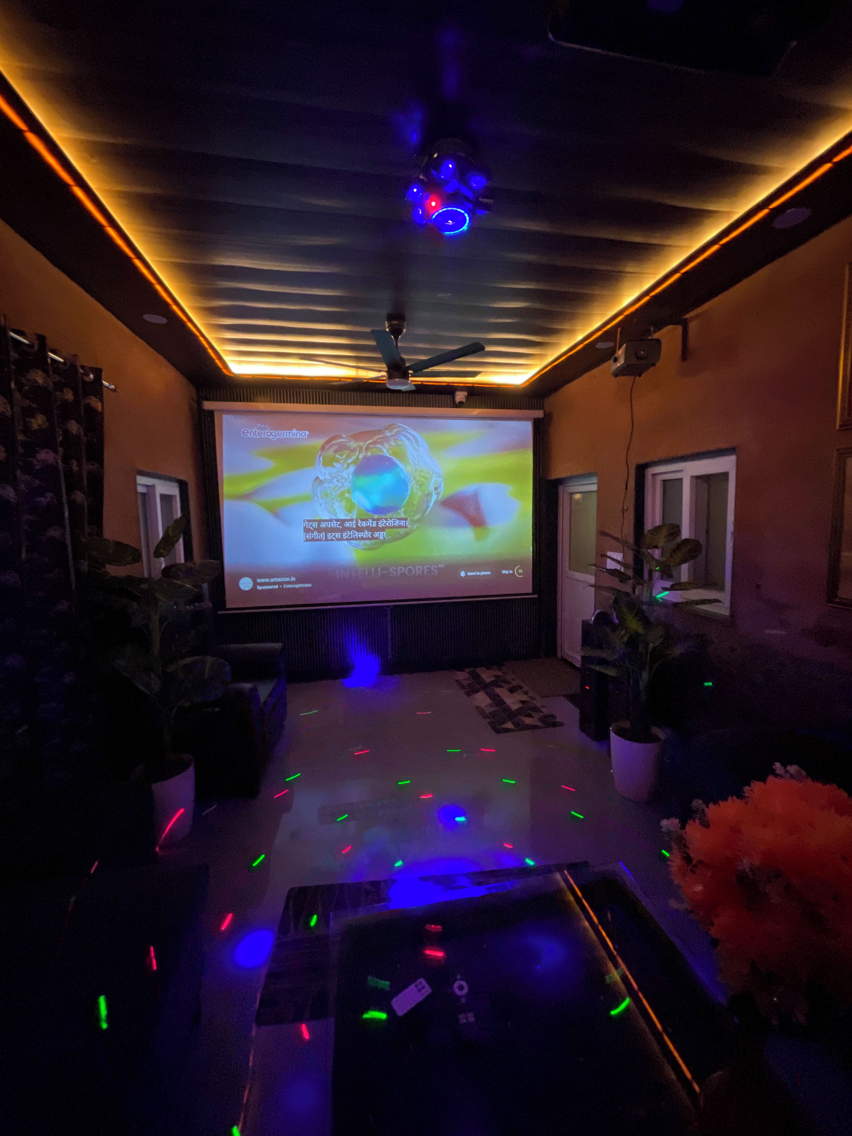A room with a large screen displaying a presentation, a ceiling fan, and a floor with colorful lights.