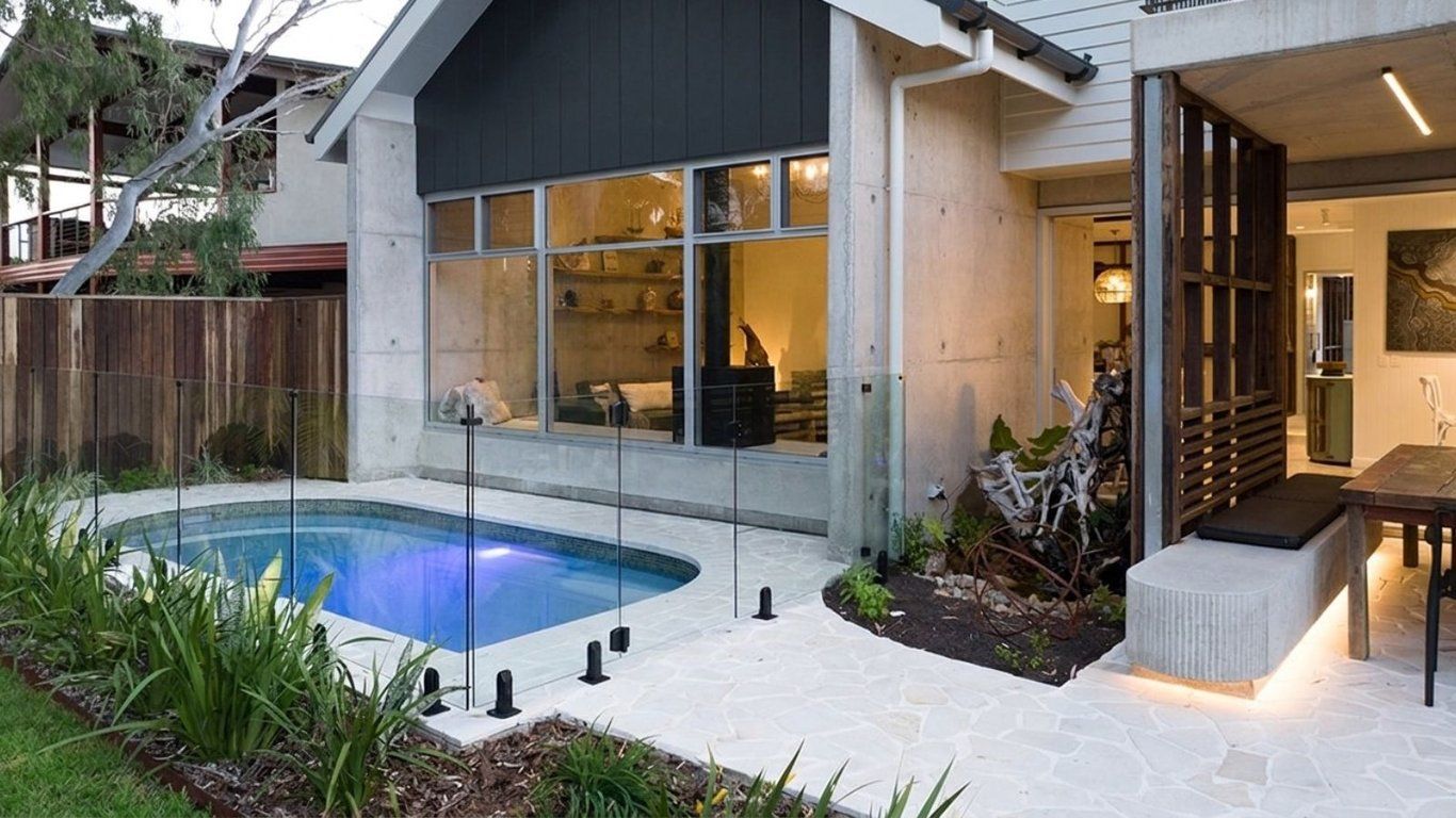 Una casa moderna con piscina, un patio cubierto y un ventanal grande con vista al jardín.