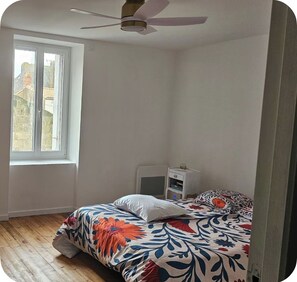 A bedroom with a bed, a nightstand, a ceiling fan, and a window. - Vrbo Property (Montréverd)
