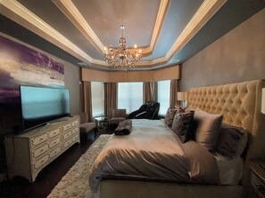 Ein Schlafzimmer mit einem großen Bett, einem Fernseher, einer Chandelüster und einem Gemälde an der Wand.