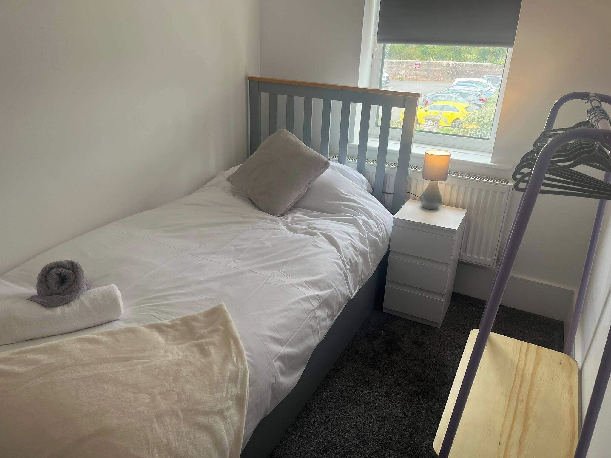 A single bed with a grey headboard, a bedside table with a lamp, a towel, and a radiator.