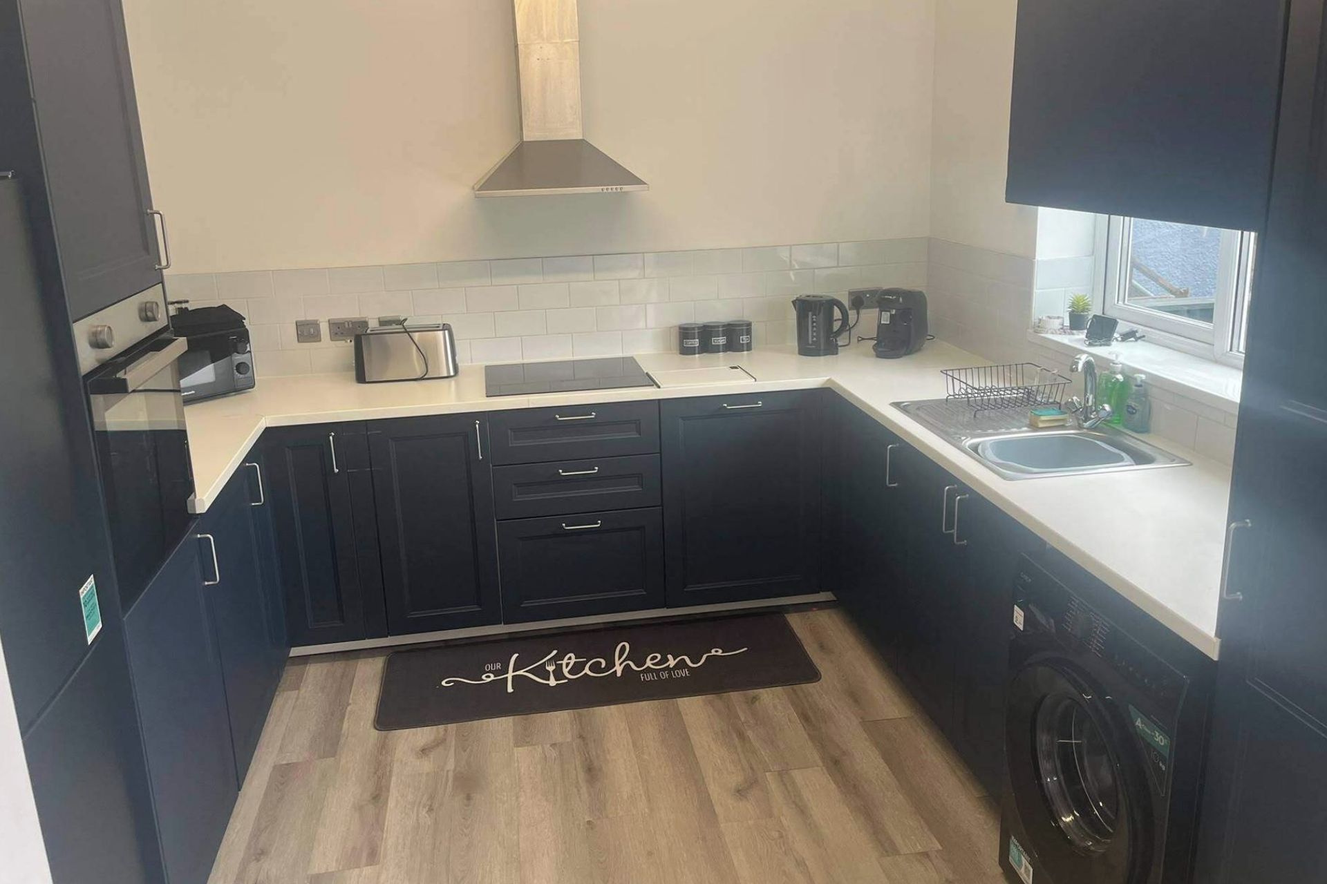 A compact kitchen with dark cabinets, a countertop, a sink, a coffee maker, and a washing machine.