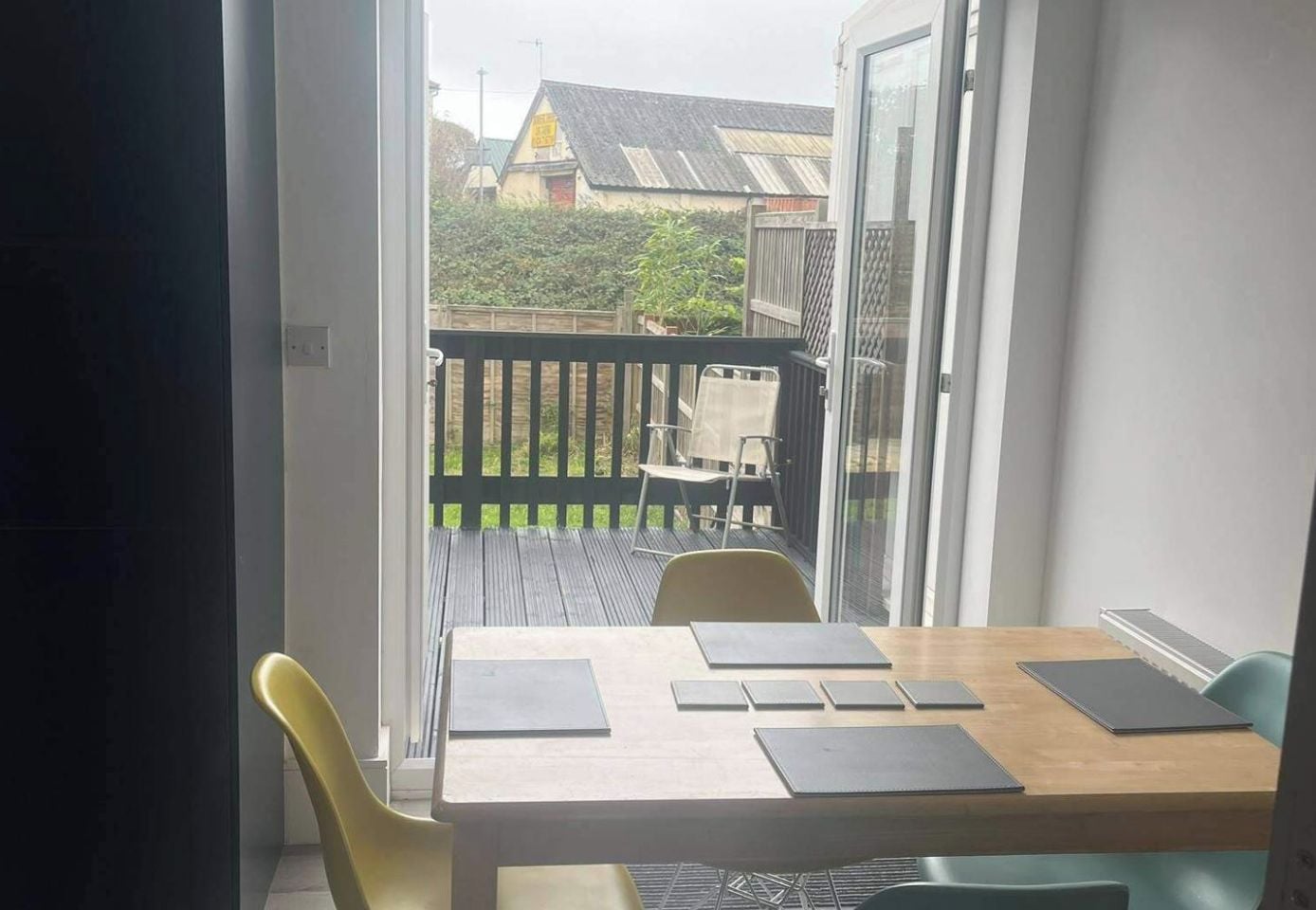 A balcony with a table and chairs, a view of a house, and a door leading outside.