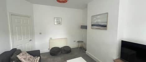A living room with a sofa, a coffee table, a television on a stand, a radiator, and a picture on the wall.
