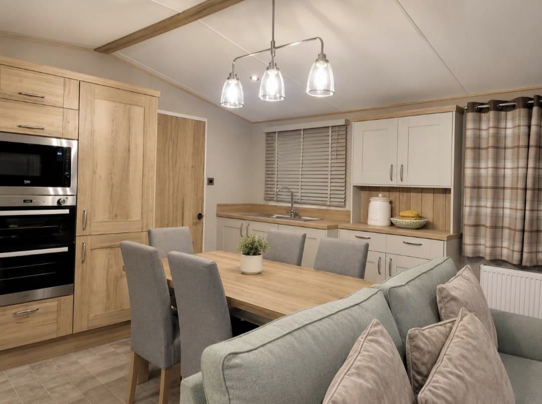 A modern kitchen with wooden cabinets, a built-in oven, and a dining area with a table and chairs.