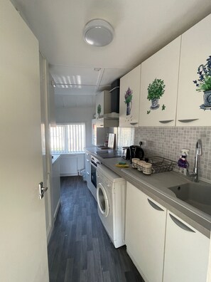 Ett kompakt kök med tvättmaskin, kaffebryggare och diskho.