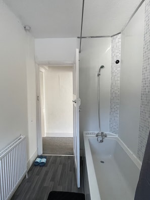 Un baño con ducha, bañera y puerta que da a otra habitación.