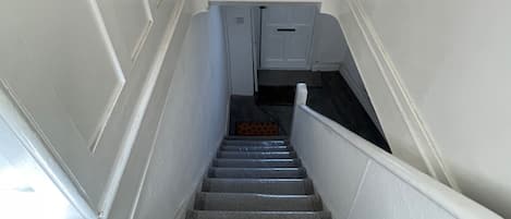 A staircase with a handrail, leading to a landing with a door and a vent.
