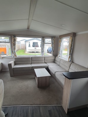 Interior de una caravana con un sofá modular, una mesita y ventanas amplias.