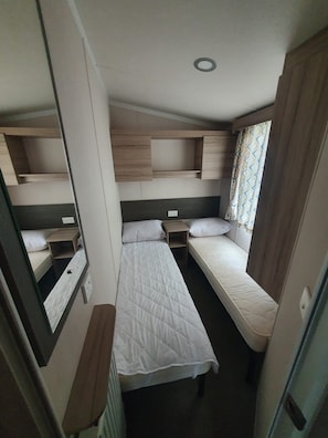 Una habitación pequeña con dos camas, una mesita y un espejo.
