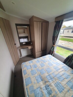 Un dormitorio con cama, armario empotrado, radiador y ventana con cortinas.