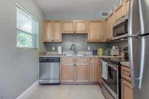 A kitchen with wooden cabinets, a stainless steel refrigerator, a dishwasher, and a microwave. - The Grounded Oak | 1mi to UT, Fenced Yard (Tampa)