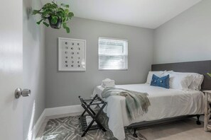 A bedroom with a bed, a window with blinds, a wall-mounted plant, and a door with a handle. - The Grounded Oak | 1mi to UT, Fenced Yard (Tampa)
