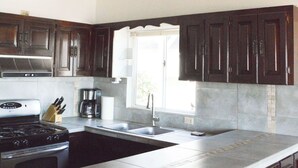 A kitchen with dark wooden cabinets, a stainless steel sink, and a built-in stove. - Playa Plateada Beach House (Ensenada)