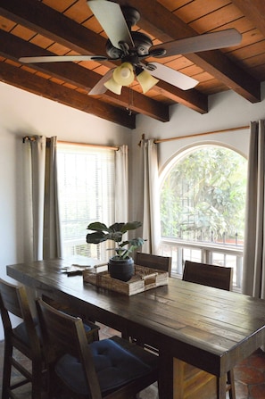 A dining area with a wooden table, chairs, a ceiling fan, and a window with curtains. - Playa Plateada Beach House (Ensenada)