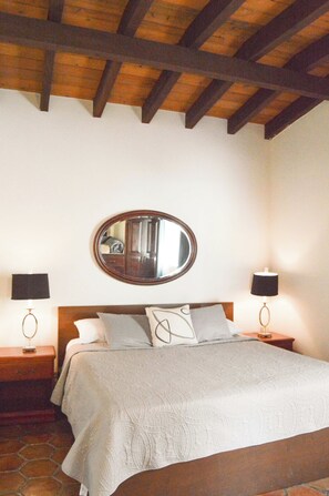 A bedroom with a bed, two bedside tables, a mirror, and a lamp on each side. - Playa Plateada Beach House (Ensenada)