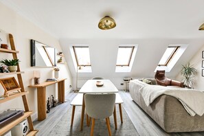 A modern loft apartment with a dining area, a sofa, and a large window providing natural light. - GuestReady - Modern & Stylish 1bed in Battersea (London)