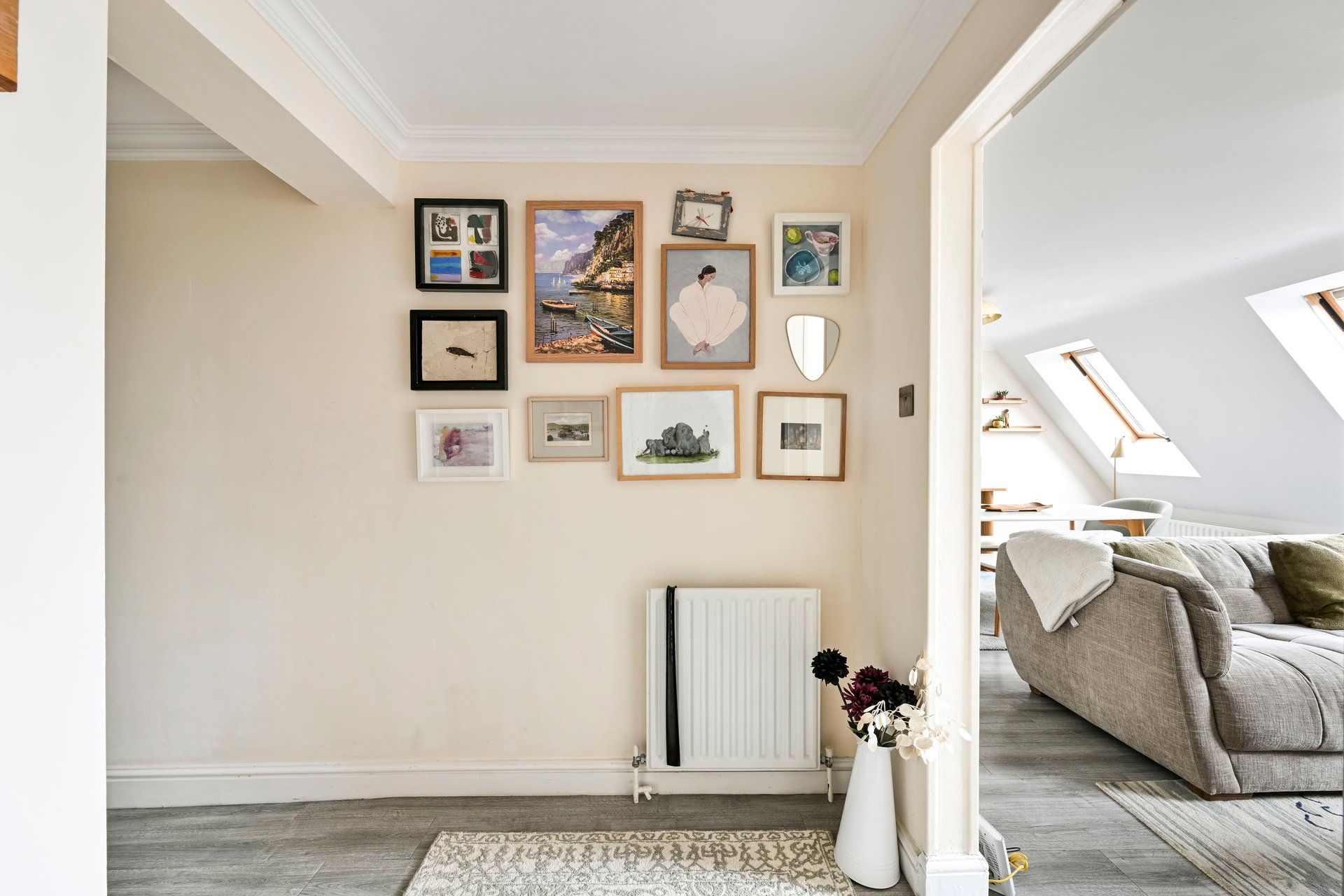 A living room with a high ceiling, a radiator, a sofa, and a wall decorated with framed pictures.