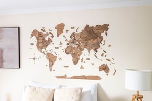 Decoração de parede com mapa-múndi e rosa dos ventos, cama com almofadas estampadas e um abajur.