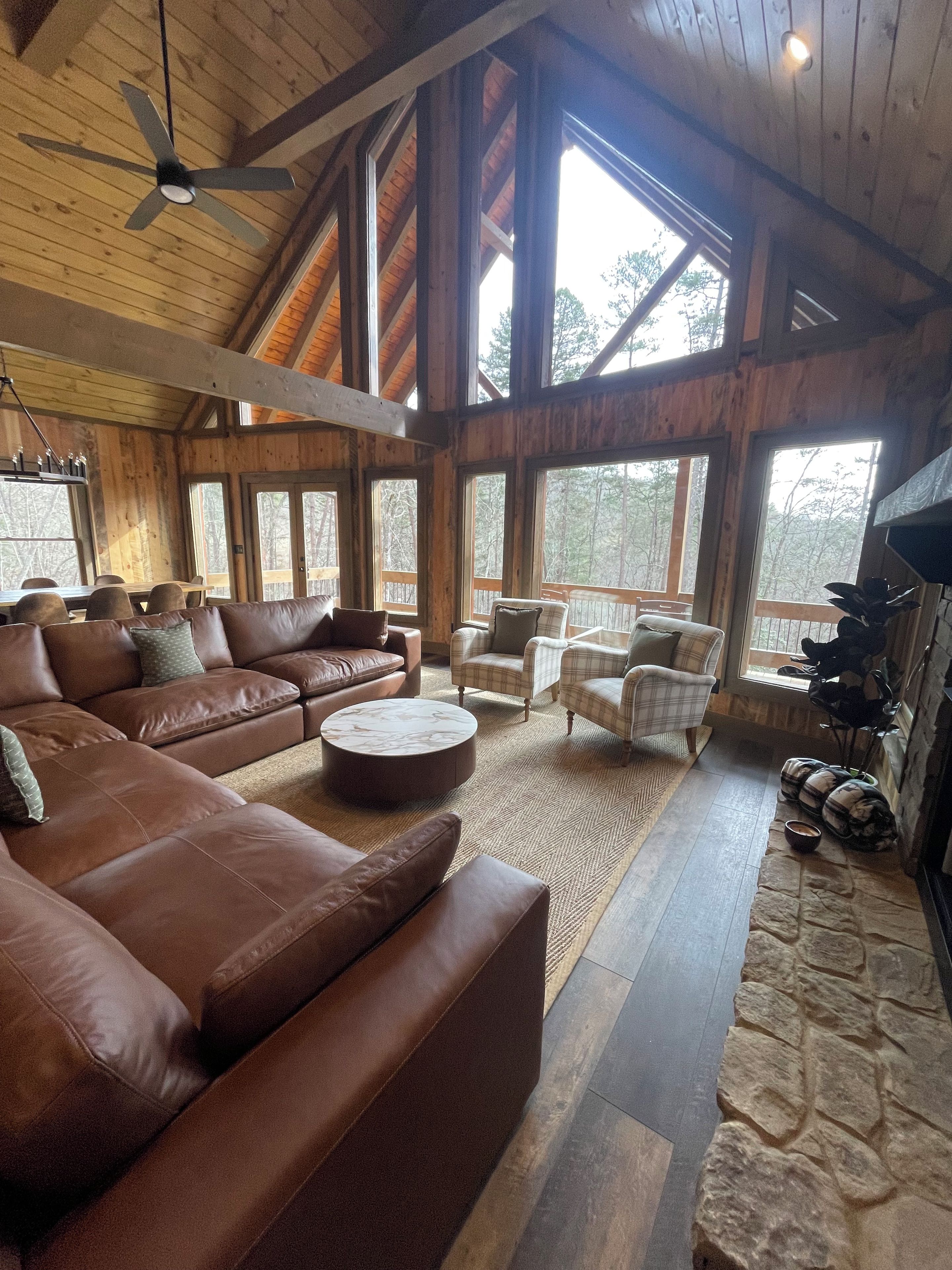 A spacious living room with a large brown leather sofa, a round coffee table, and plaid armchairs.