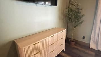 Een kamer met een houten vloer, een lichtkleurige kast, een potplant en een flatscreen televisie aan de muur.