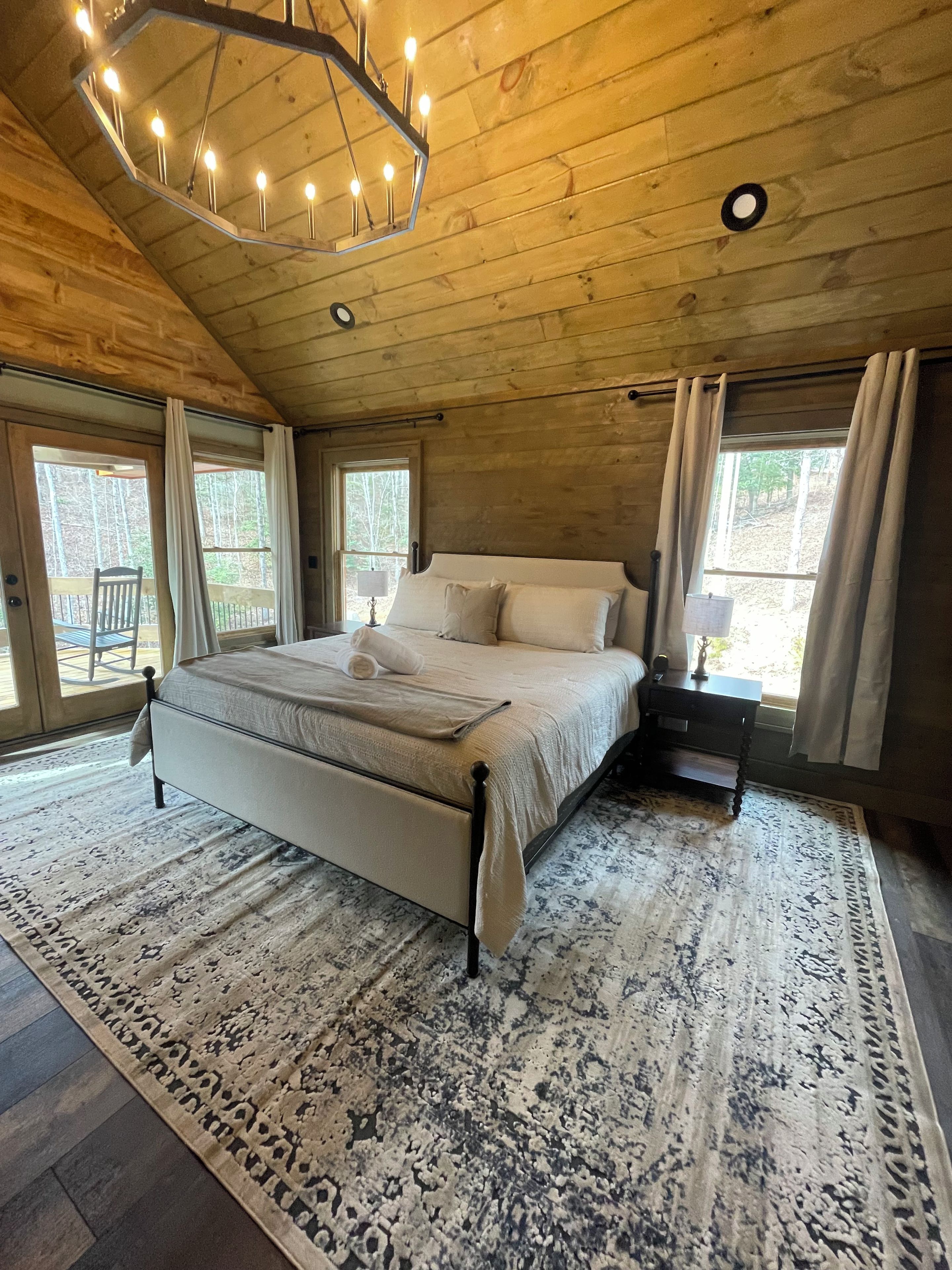 A bedroom with a bed, nightstand, and a large window.