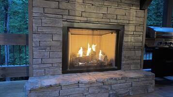 A stone fireplace with a glass screen, set in a wooden deck with a view of trees.