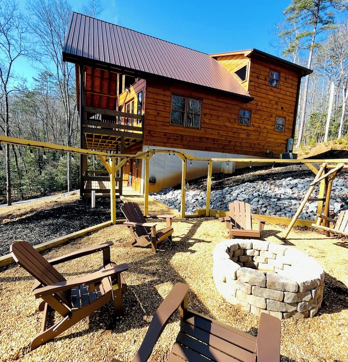 A wooden cabin with a deck, outdoor seating, and a fire pit.