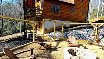 A wooden cabin with a deck, outdoor seating, and a fire pit.