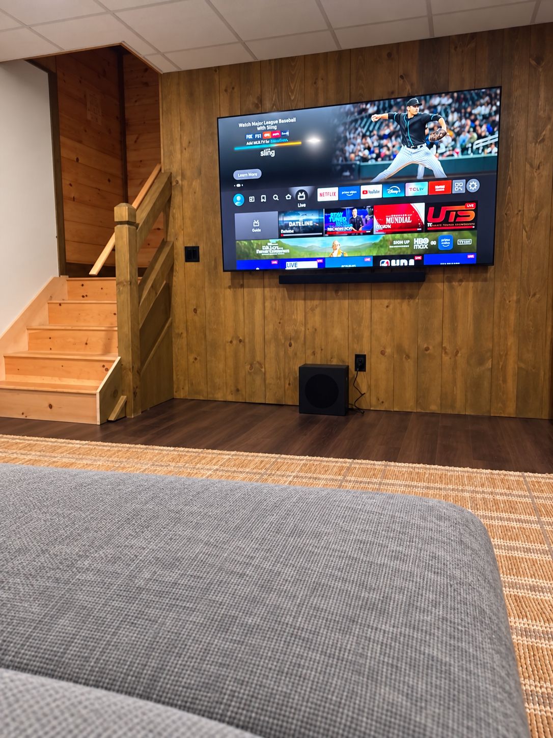 A flat-screen TV mounted on a wooden wall with a wooden staircase to the left.