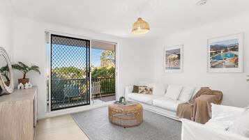 A modern living room with a white sofa, a round wicker coffee table, and a balcony with a view.