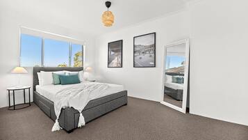 A modern bedroom with a large bed, two bedside tables, a hanging light fixture, and a view through a door.