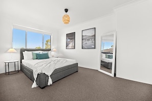 A modern bedroom with a large bed, two bedside tables, a hanging light fixture, and a view through a door. - Stylish 3 bedroom apartment in Miranda steps to Westfield and train station. (Miranda)