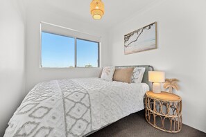 A bedroom with a large window, a bed with patterned bedding, a bedside lamp, and a wall-mounted picture.