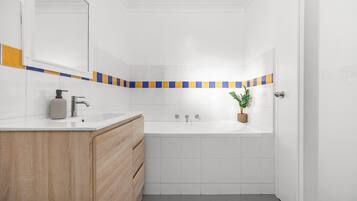 A bathroom with a white sink, wooden vanity, and a bathtub.