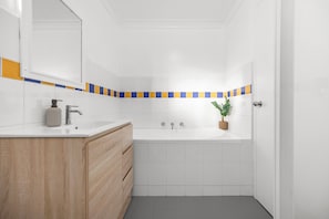 A bathroom with a white sink, wooden vanity, and a bathtub. - Stylish 3 bedroom apartment in Miranda steps to Westfield and train station. (Miranda)