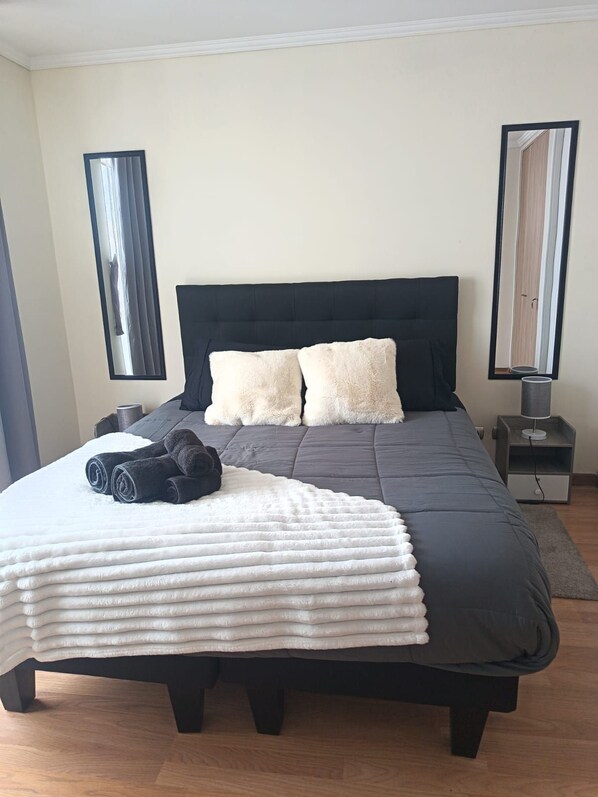 A neatly made bed with a black headboard, two white fluffy pillows, and a white textured blanket. There are two rolled-up towels on the bed. - A cozy and comfortable apartment in San Miguel, just steps from the subway. (San Miguel)