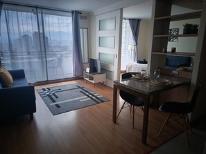 A modern living room with a sofa, a dining table, and a kitchen area with a bed and a window. - A cozy and comfortable apartment in San Miguel, just steps from the subway. (San Miguel)