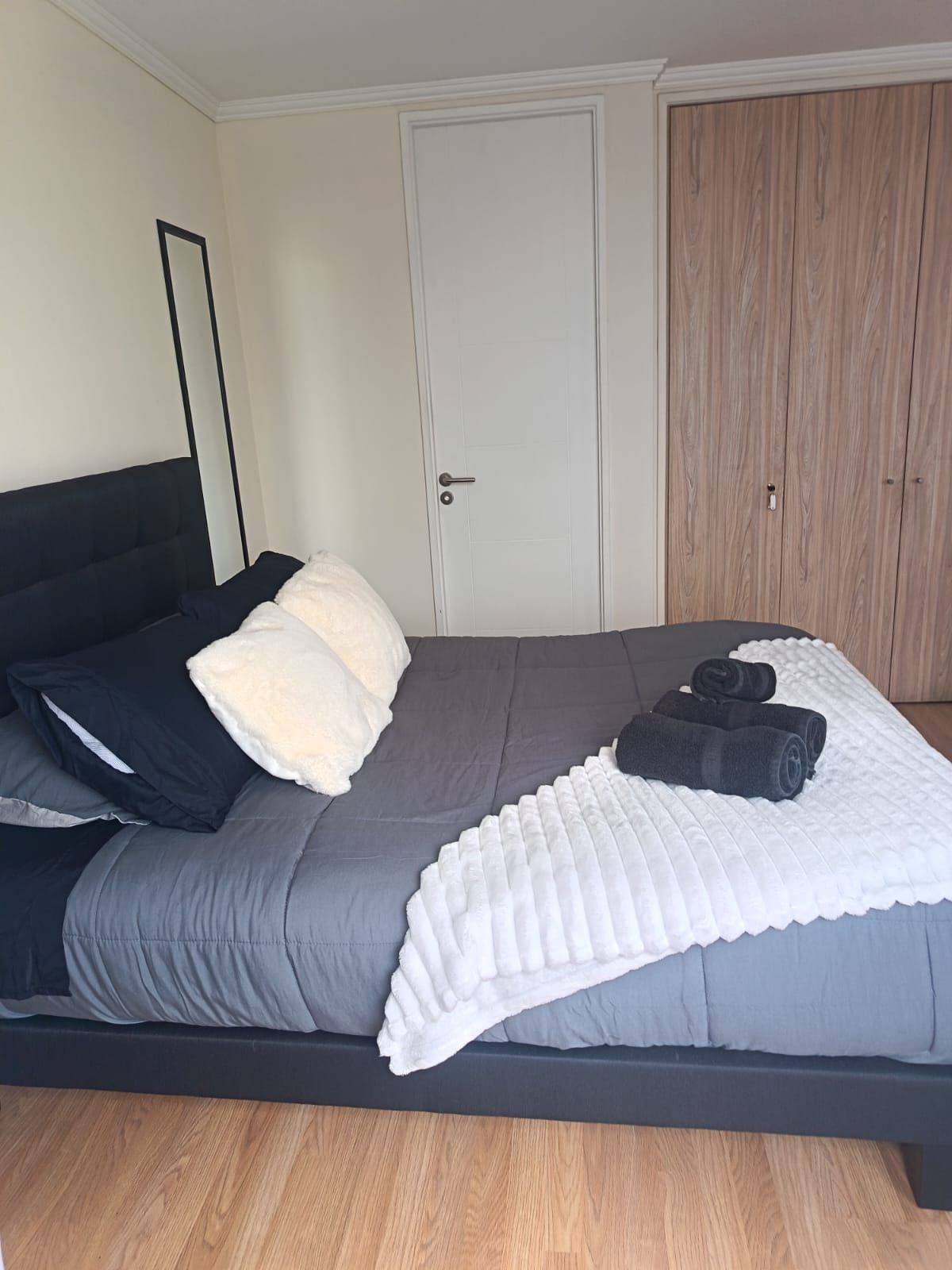 A bedroom with a bed, pillows, a blanket, and a rolled towel.