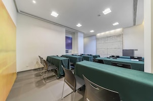 Un salón de conferencias con mesas y sillas, una pantalla de proyector y una pizarra.