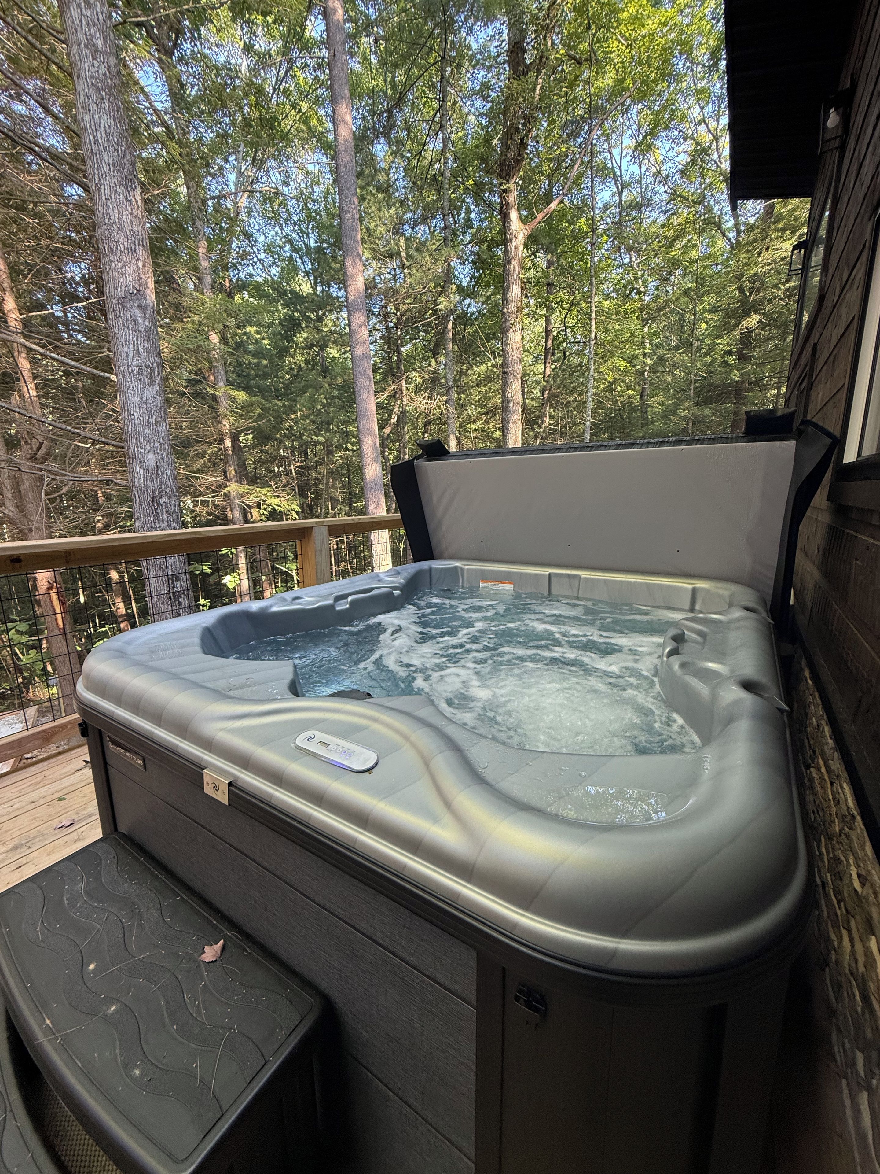 A hot tub on a wooden deck with a view of a forest.
