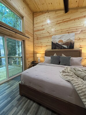 A wooden-paneled bedroom with a bed, pillows, a nightstand, a lamp, and a painting.